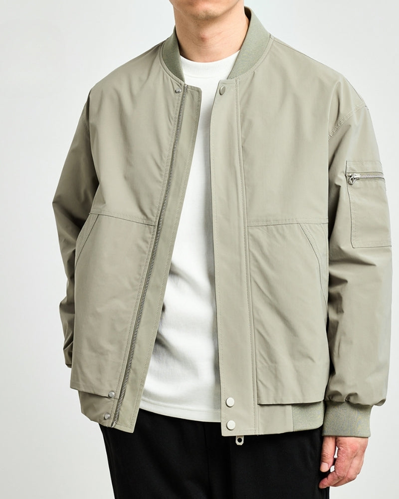 Man in sage-green bomber jacket unzipped over a white tee and black trousers, front view