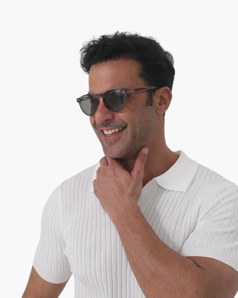 Smiling man in round tinted sunglasses and white ribbed polo, hand on chin