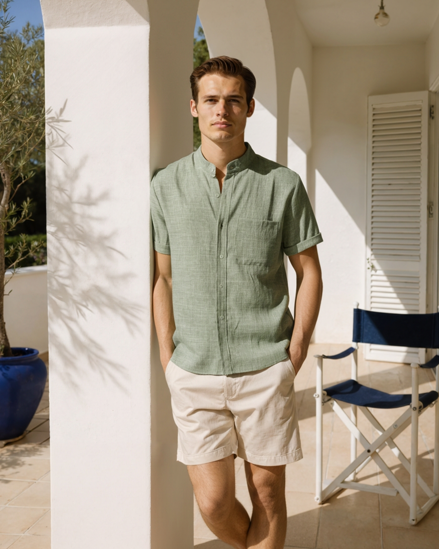 Sage green mandarin-collar short-sleeve shirt with chest pocket, worn with beige shorts on a terrace