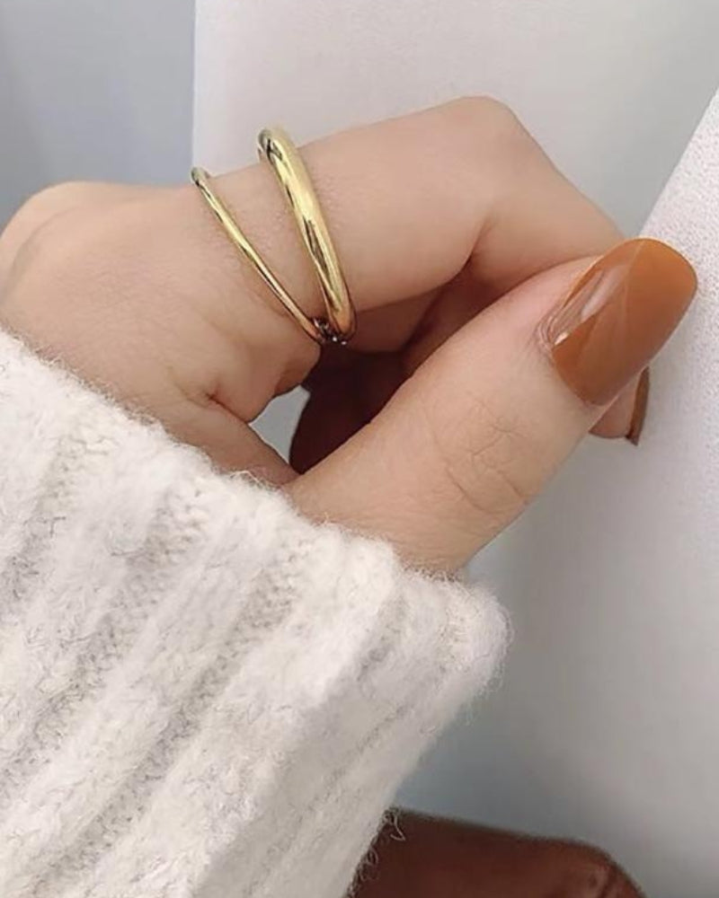 Anillo doble dorado en el dedo, mano apoyada sobre una manga de punto blanca