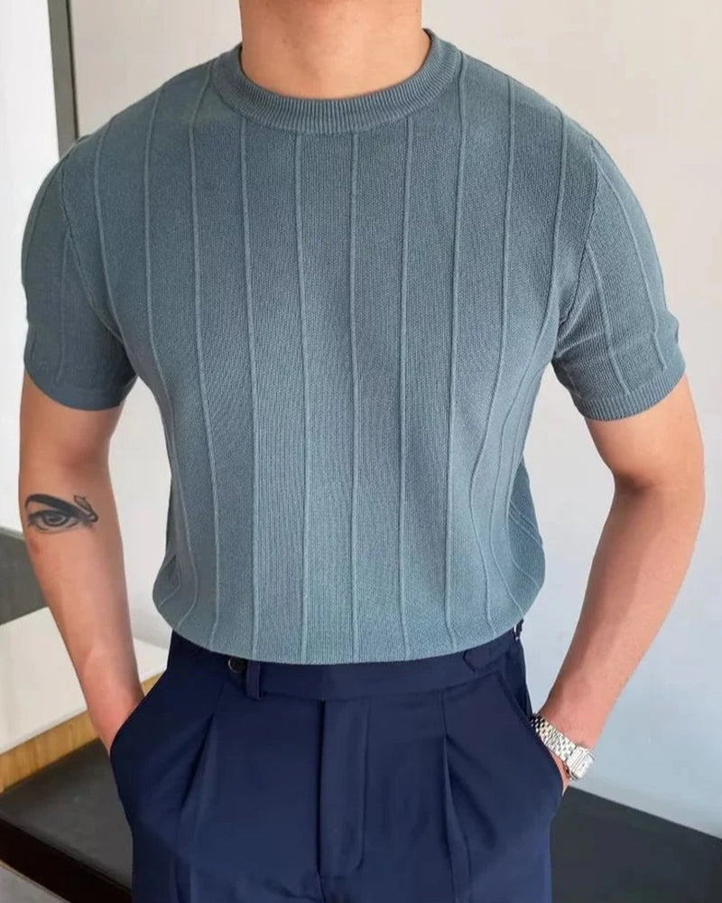Man in a blue-grey ribbed knit crewneck tee with navy trousers, hands in pockets