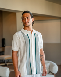 Man in a white knit polo with grey and green vertical stripe panels down the placket, front view