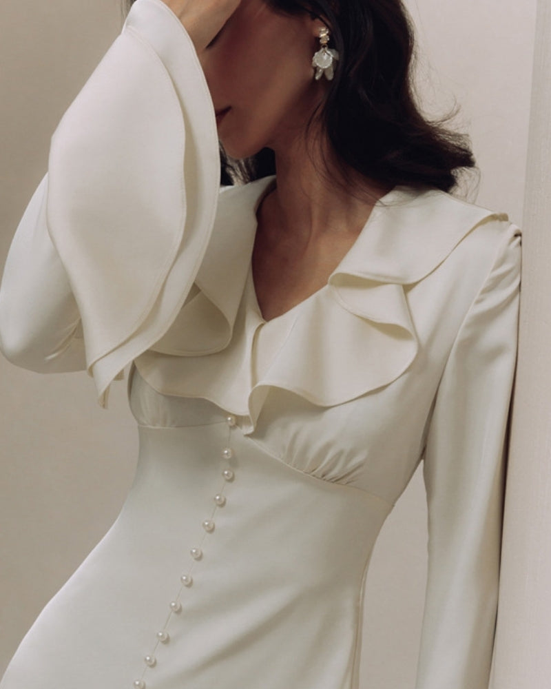 Close-up of ivory dress V-neck ruffle collar, bell sleeve and pearl button placket on model