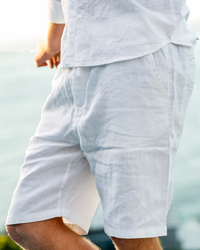Primer plano de unos shorts de lino blancos con cordón, con camisa blanca junto al mar