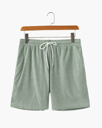 Sage-green ribbed corduroy drawstring shorts with white cord and elastic waist, front view on a wooden hanger