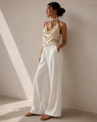 Woman in white wide-leg trousers, champagne satin cowl camisole and silk scarf at the neck, side view