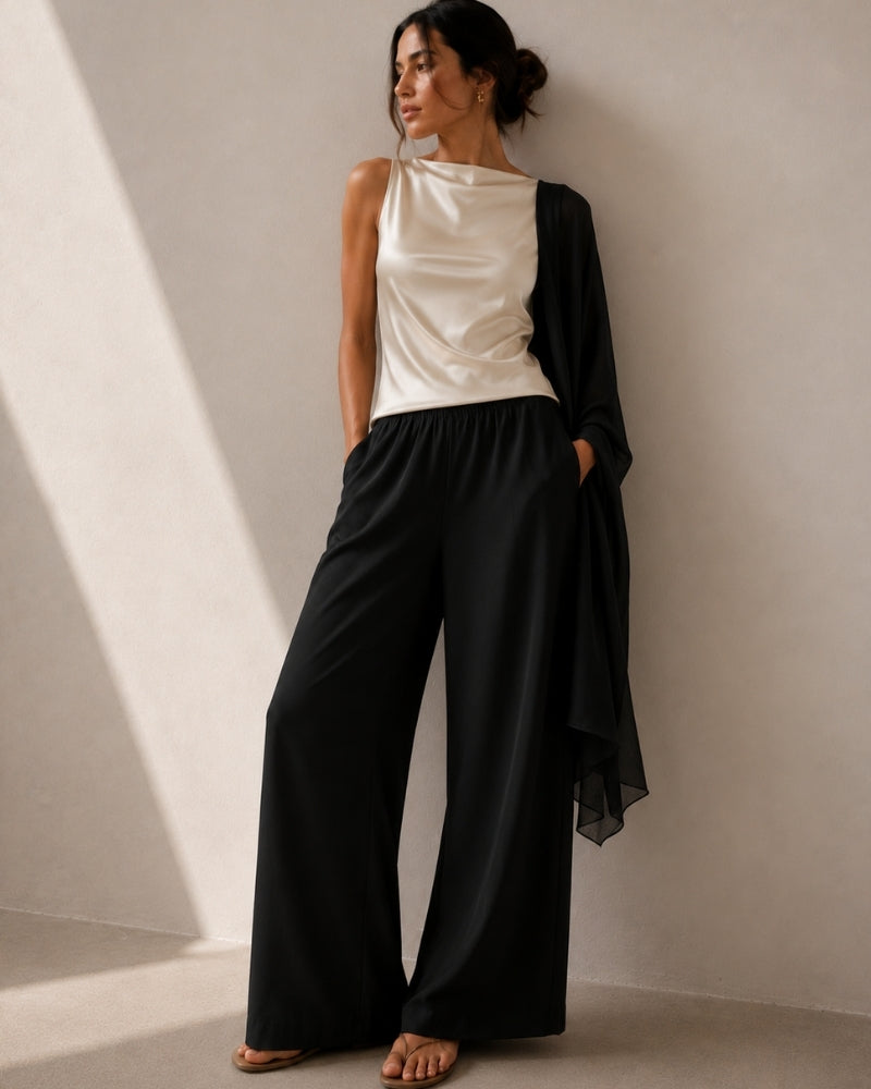 Woman in black wide-leg trousers, ivory satin top and black sheer shawl draped over one arm