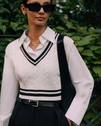 Woman in sunglasses wearing cream cable-knit V-neck vest with black stripes over a white shirt