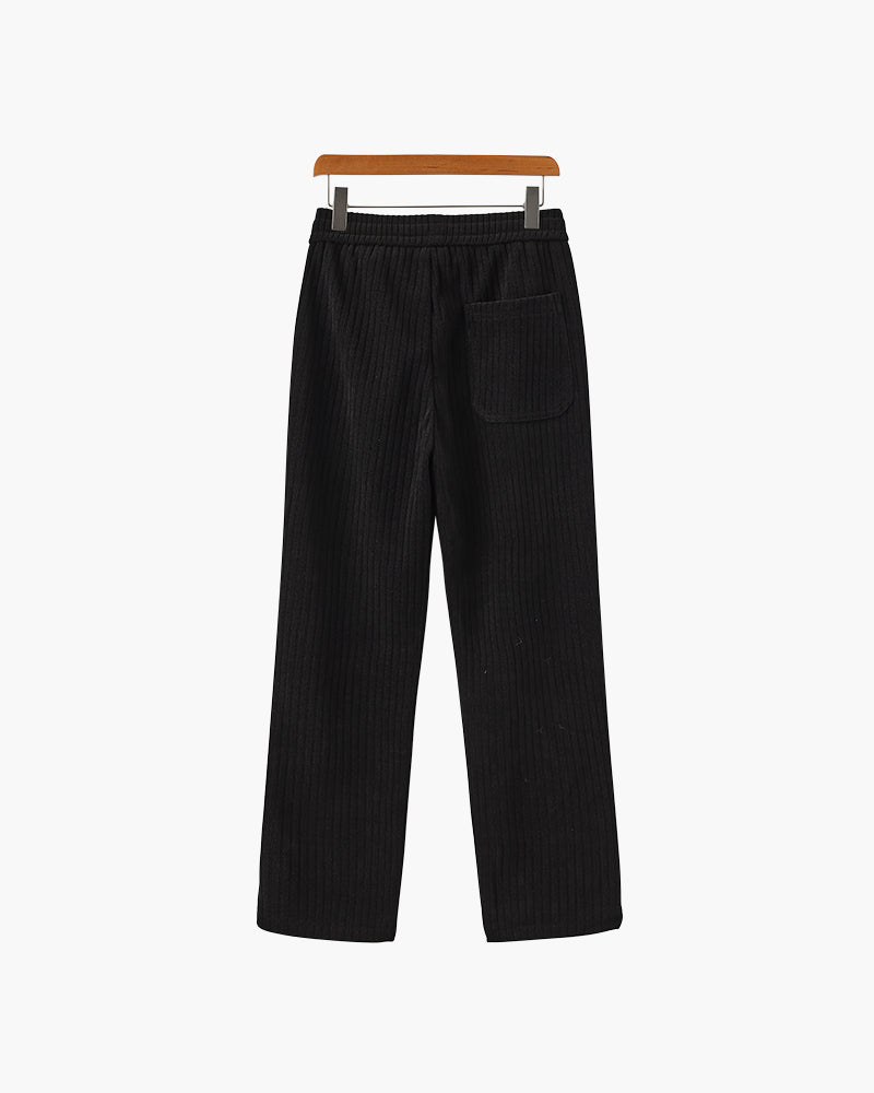 Back view of black ribbed velvet trousers with elastic waist and patch back pocket, on a wooden hanger