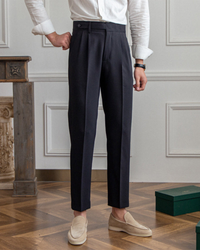 Man in dark navy high-waisted pleated trousers, white linen shirt and sand suede loafers, front view