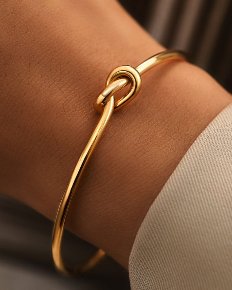 Primer plano de un brazalete de nudo dorado en la muñeca junto a una manga cruda