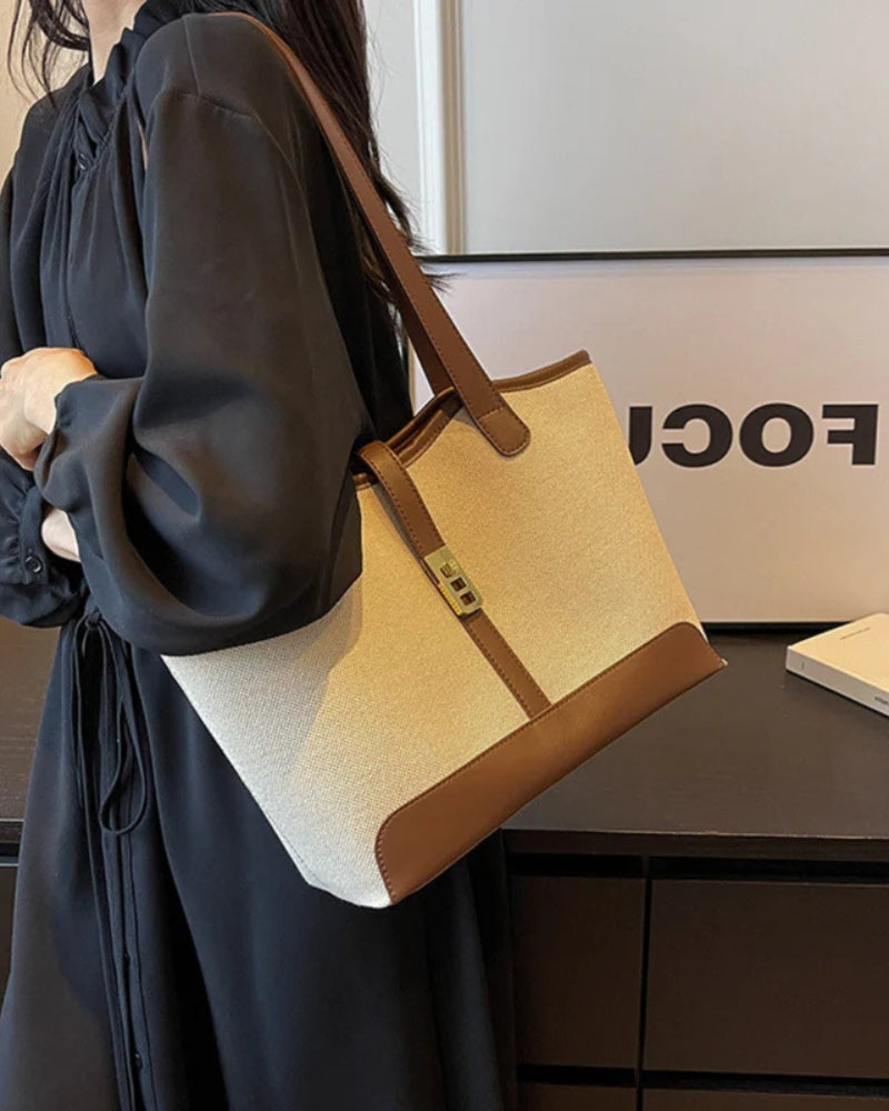 Beige canvas tote with brown leather trim carried on the shoulder, worn with a black dress