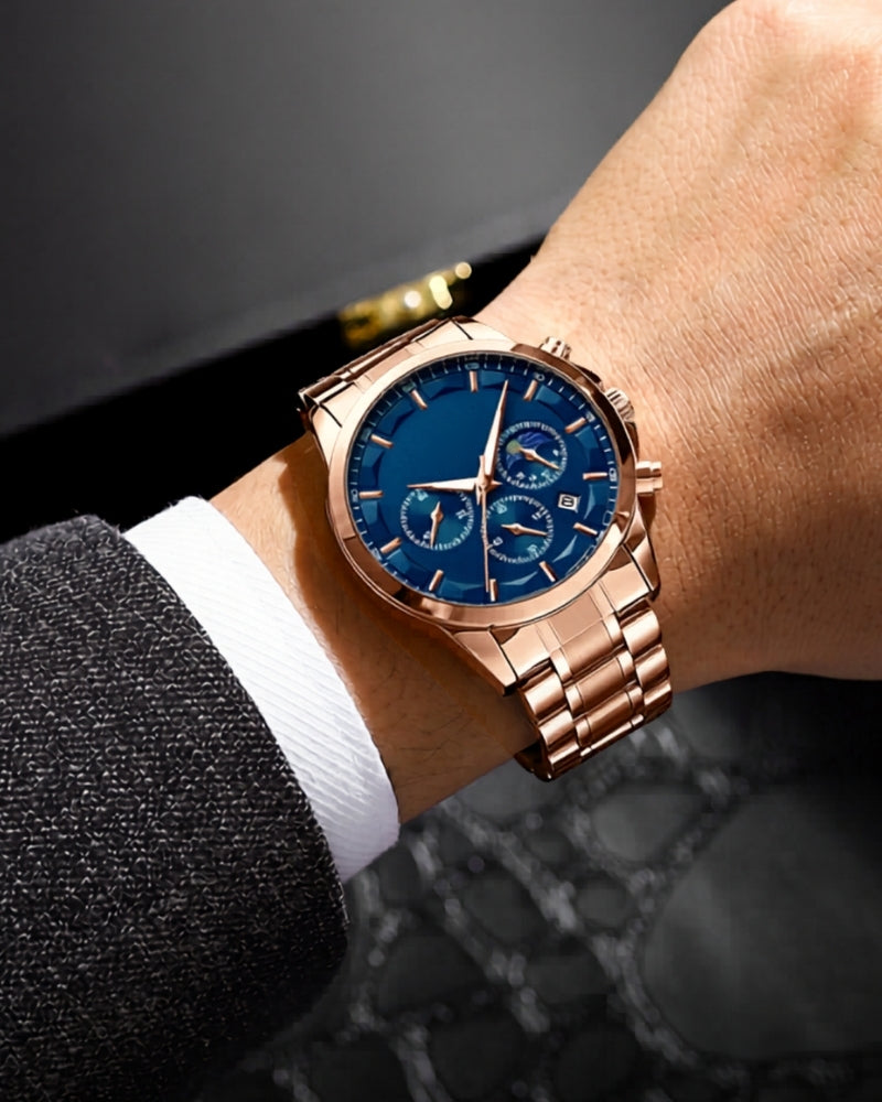 Rose-gold chronograph watch with blue dial on a man's wrist, with suit sleeve and white shirt cuff