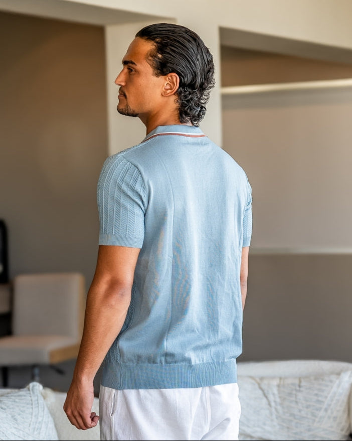 Vue de dos de trois quarts d'un polo en maille côtelée bleu clair à ourlet côtelé, porté avec un pantalon blanc