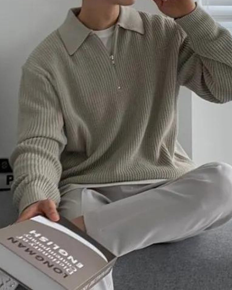 Man wearing sage grey ribbed half-zip jumper, seated and holding a book