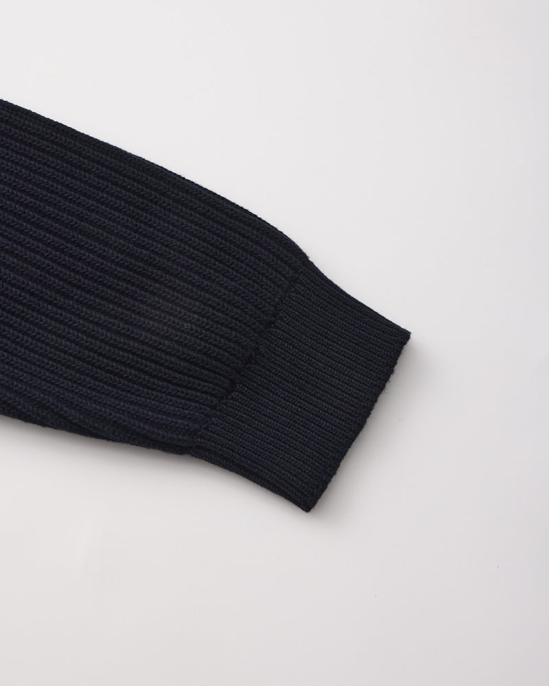 Close-up of navy rib-knit jumper sleeve end with ribbed cuff, flat-lay on white