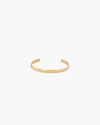 Gold-tone polished open cuff bracelet with a slim flat band, front view on white