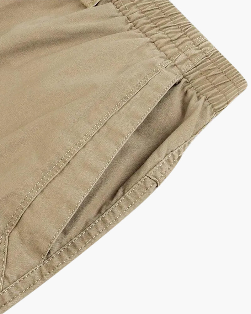 Close-up of a khaki elasticated waistband and side pocket seam, flat on white