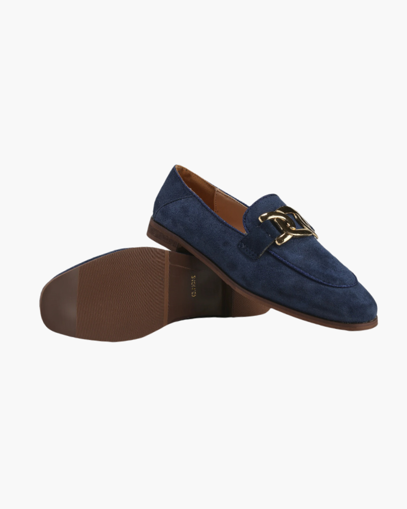 Navy blue suede loafer flat-lay with gold chain detail and brown sole turned beside it