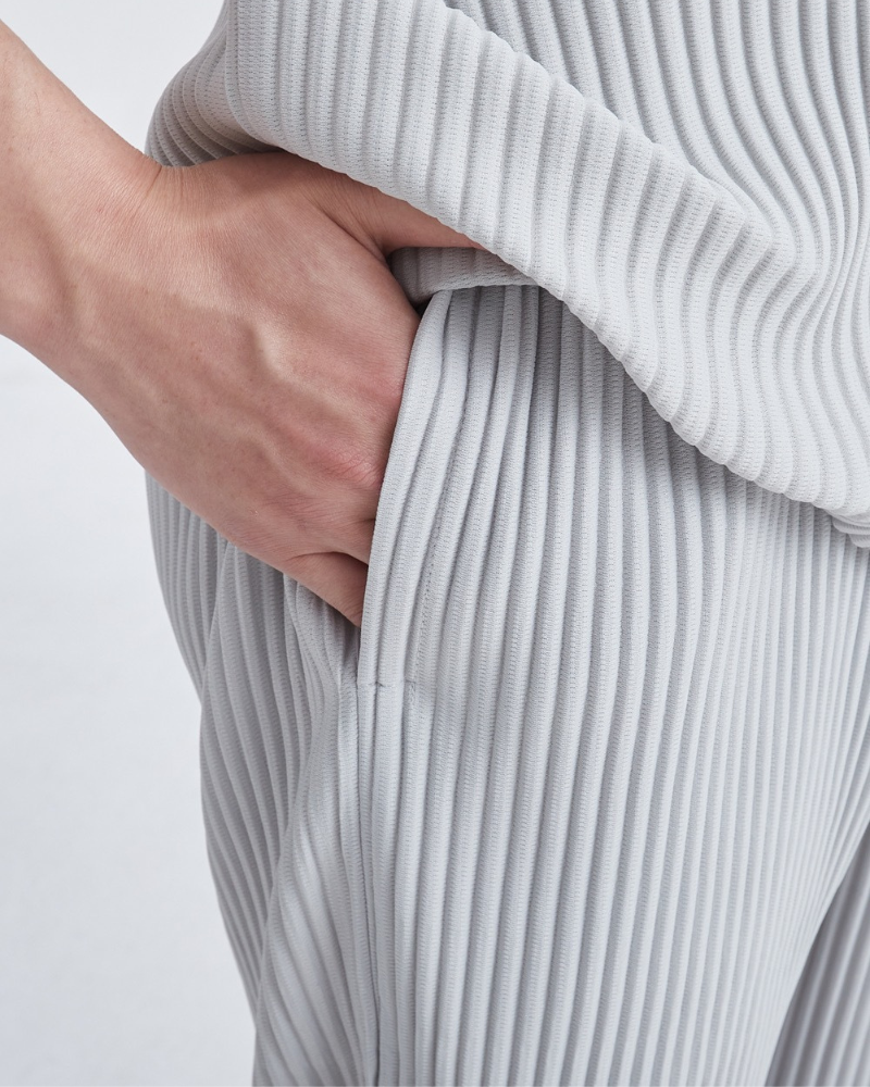 Close-up of hand in the side pocket of light grey fine-pleated trousers and matching top