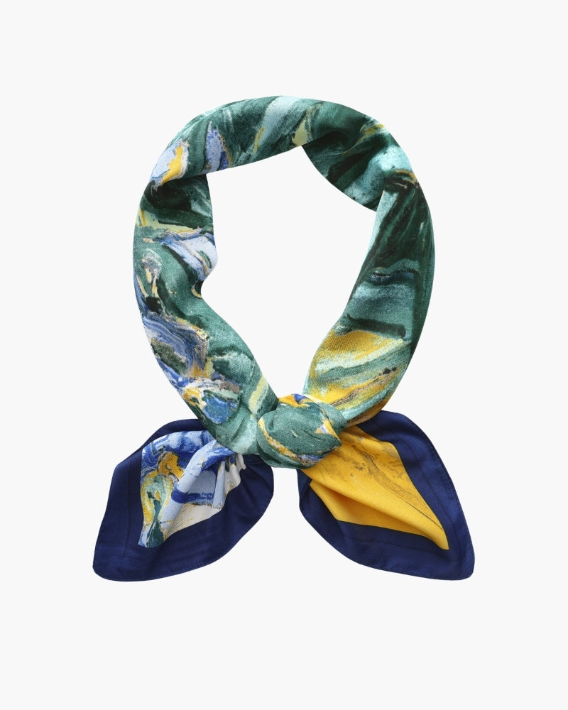 Painterly blue-green and yellow scarf knotted in a loop with navy corners, flat-lay