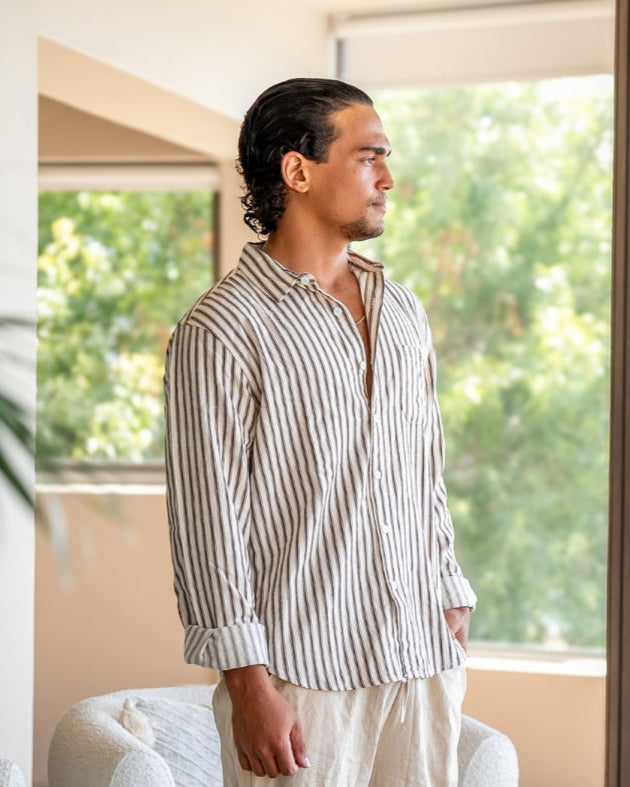 Man in brown striped shirt with sleeves rolled, side view by a sunlit window