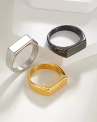 Rectangular signet rings in silver, black and gold finishes on a cream surface
