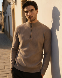 Man in a taupe cashmere half-zip jumper leaning on a sunlit wall, front view with ribbed panels