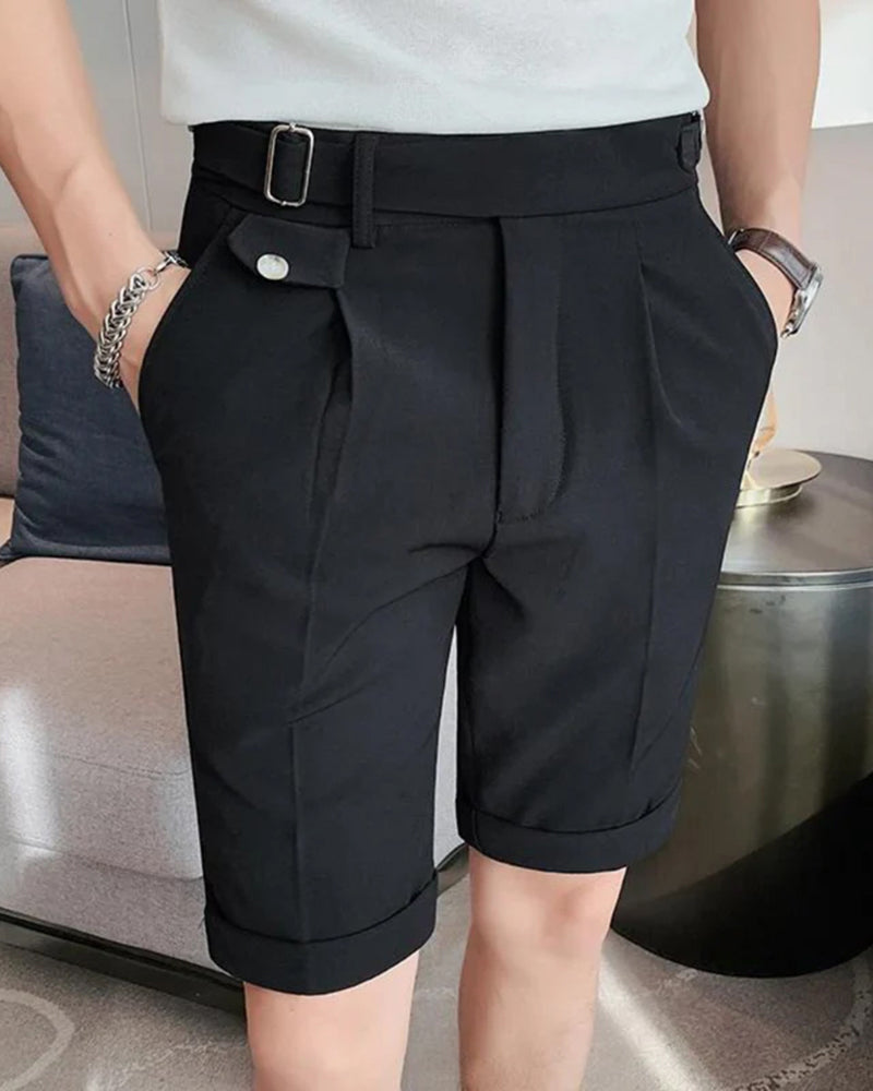 Mann in schwarzen Bundfaltenshorts mit silberner Schnallenlasche am Bund und Umschlag, weißes T-Shirt, Hände in den Taschen