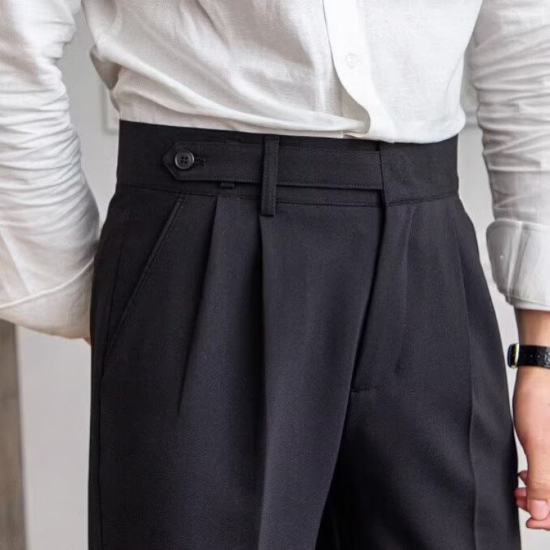 Close-up of black trousers waist with side-adjuster button tab, double pleats and slanted pocket on model