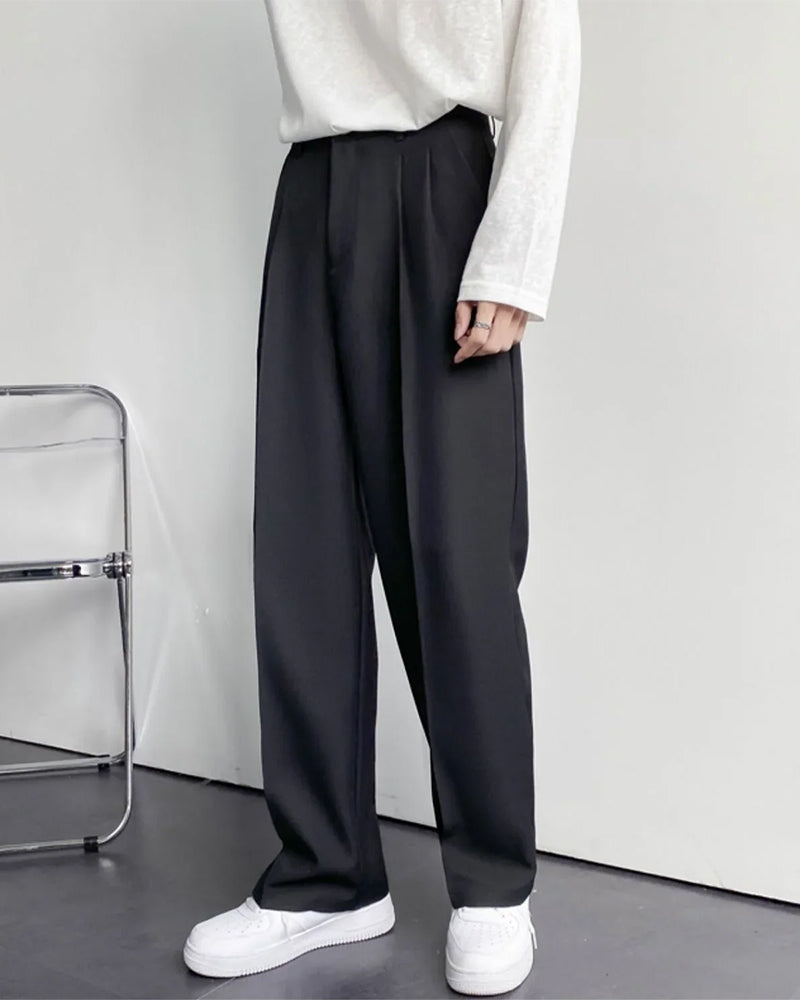 Man wearing dark grey pleated wide-leg trousers with white sneakers, side angle