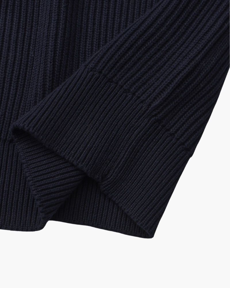 Close-up of navy rib-knit jumper sleeve folded to show the ribbed cuff and chunky rib texture