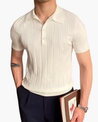 Man in a cream ribbed knit short-sleeve polo with navy trousers, holding a book