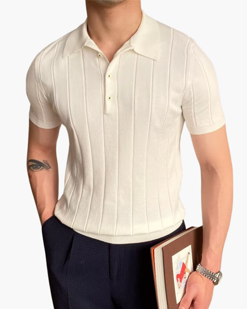 Man in a cream ribbed knit short-sleeve polo with navy trousers, holding a book