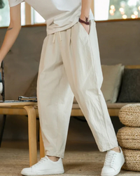 Model's lower half in cream linen-cotton drawstring trousers with a white tee and trainers