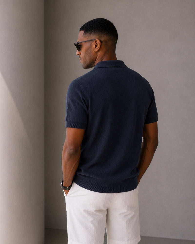 Back view of man in navy knit polo with white trousers and sunglasses