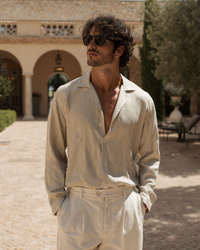 Man in brown and cream striped shirt worn open-necked with sunglasses, courtyard setting