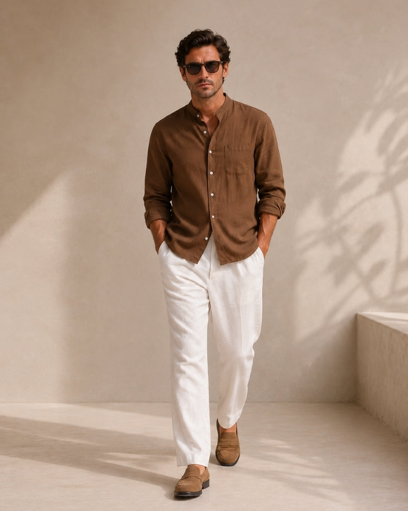 Man in sunglasses wearing brown mandarin collar shirt and white trousers, hands in pockets