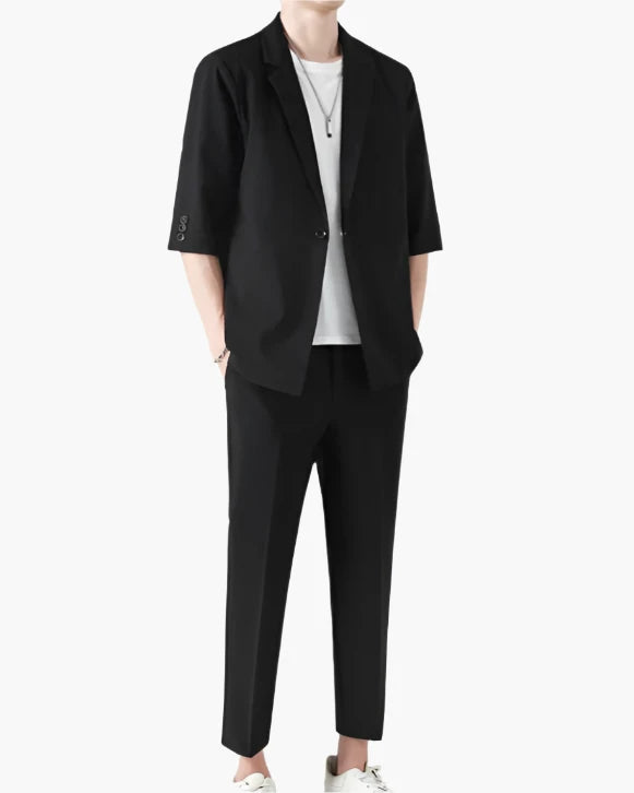 Man wearing black half-sleeve blazer, white tee and black cropped trousers, hands in pockets