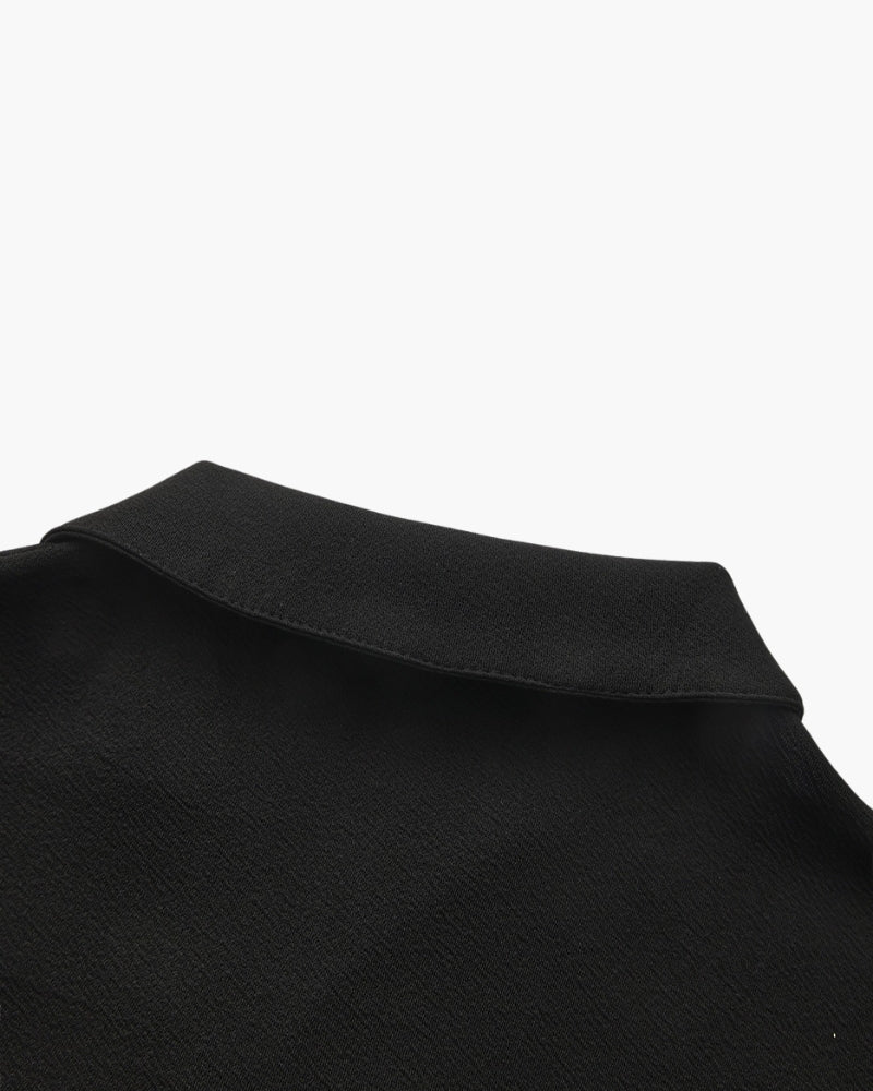 Close-up of a black textured polo collar at the back neck, flat on white