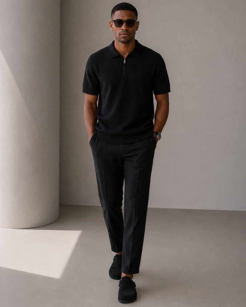 Man in sunglasses walking in black knit zip polo and black trousers