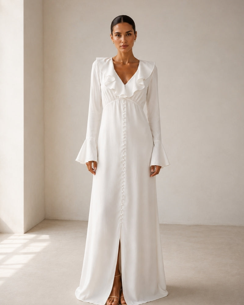 Front view of woman in ivory ruffle-collar maxi dress with pearl button front, bell cuffs and front slit