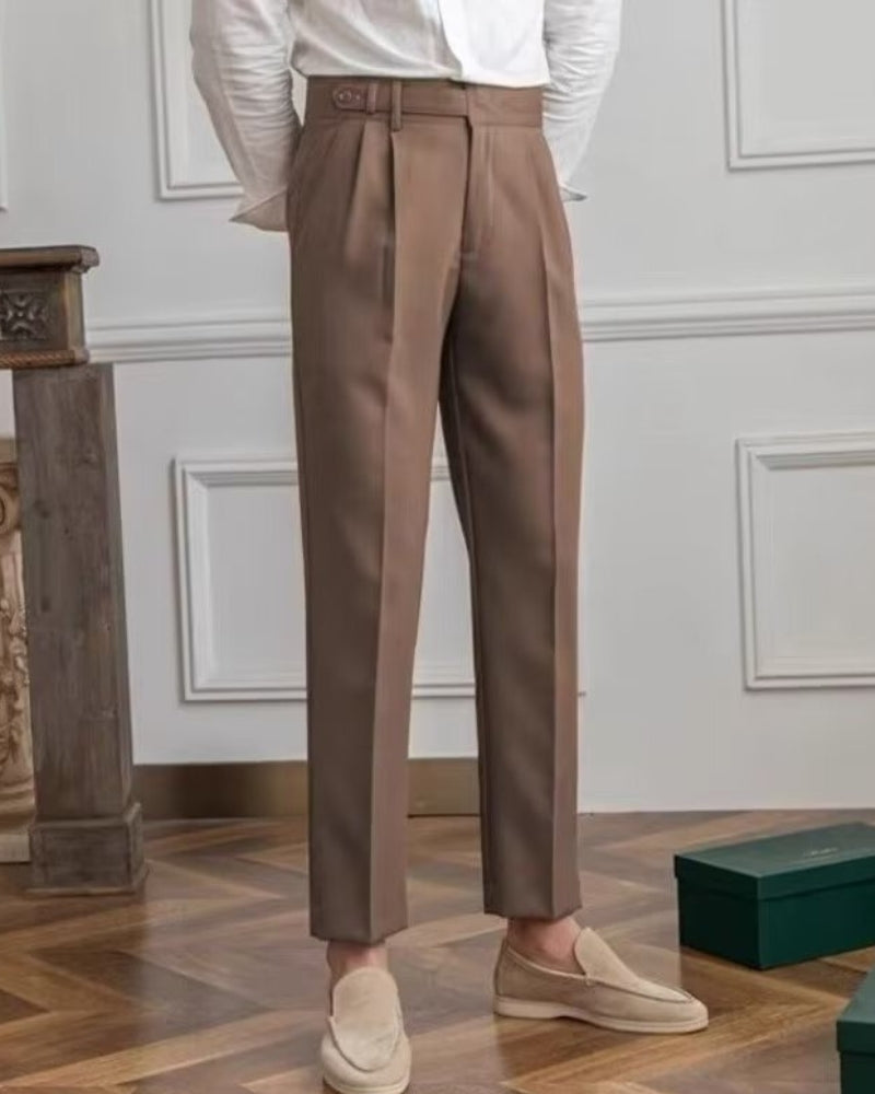 Man in brown high-waisted pleated trousers, white shirt and sand suede loafers, front view