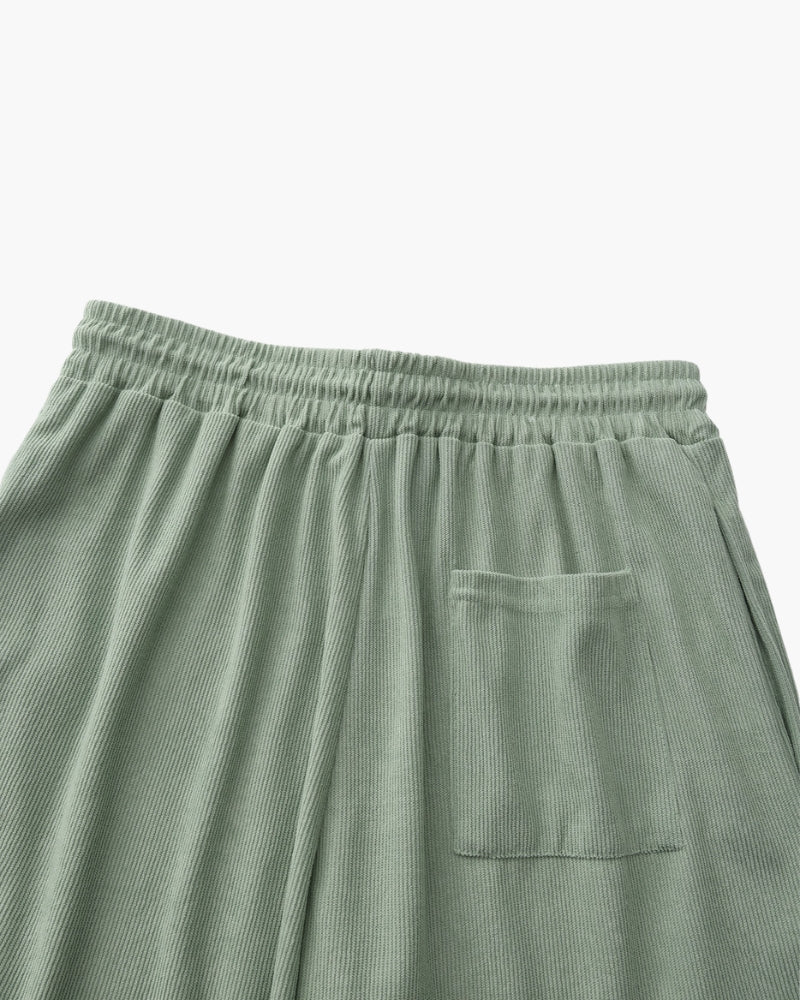 Back view of sage-green ribbed corduroy shorts with elastic waist and patch back pocket, flat-lay