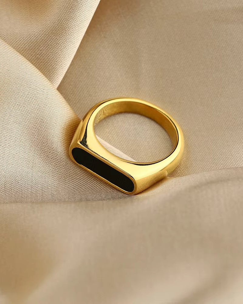 Gold-tone band ring with a long black enamel inlay, angled view on beige satin