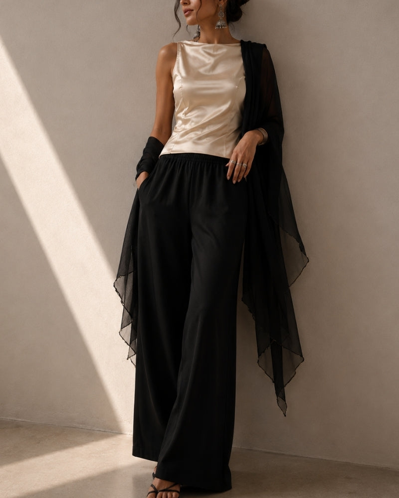 Femme en pantalon large noir, top en satin champagne et châle noir transparent, cadrée sous le visage