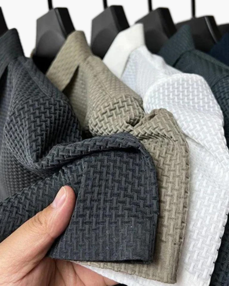 Hand hält gestapelte Waffelstrick-Polos in Anthrazit, Khaki, Weiß und Marineblau auf Bügeln