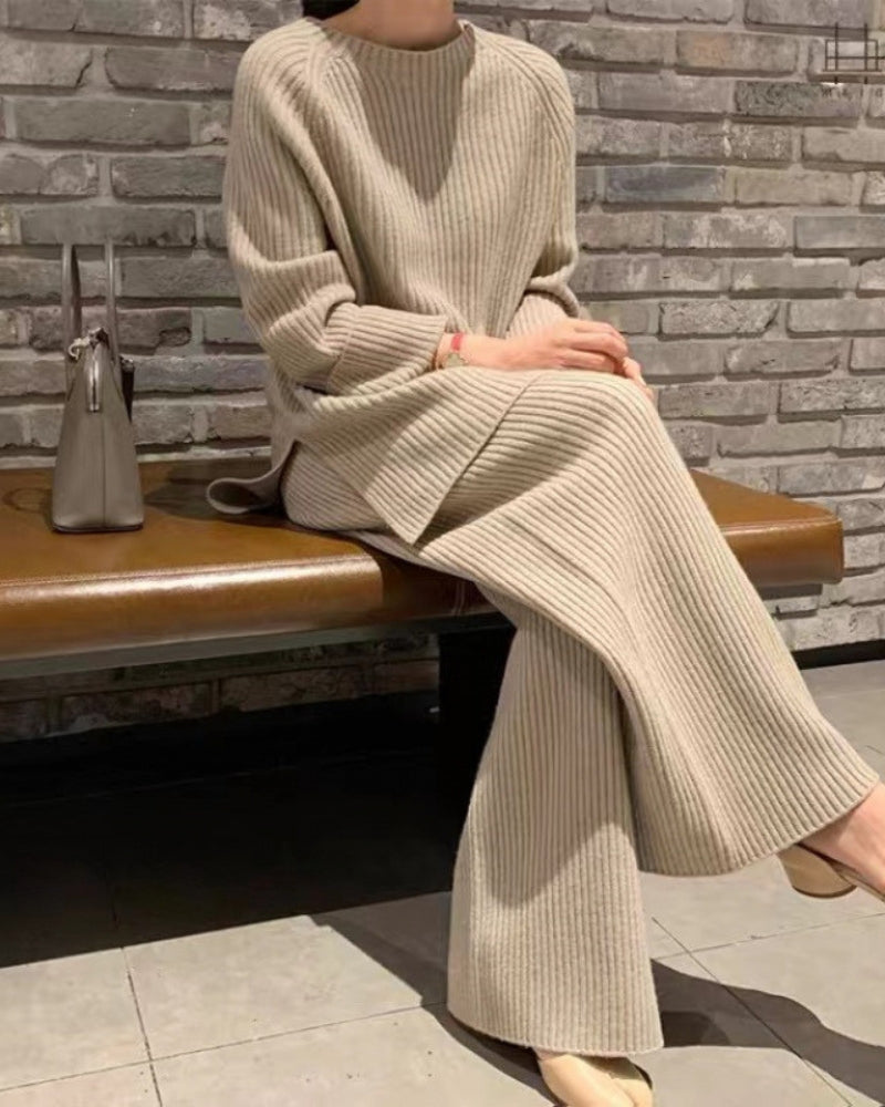 Woman seated on a bench in a beige ribbed knit lounge set with side-slit jumper and wide-leg trousers