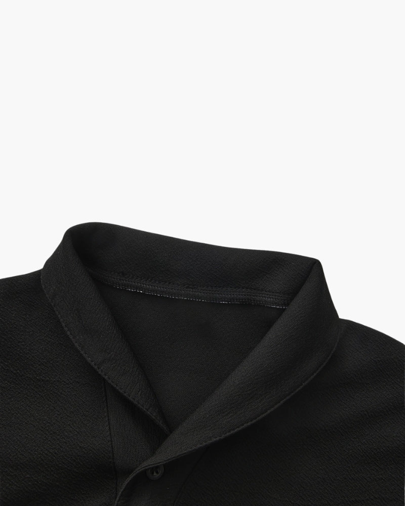 Close-up of a black polo's folded collar and textured fabric, flat on white