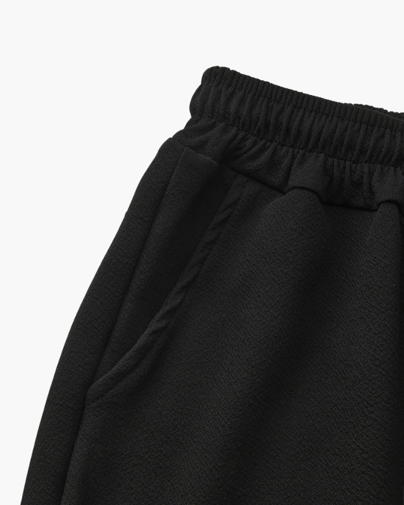 Close-up of a black elasticated waistband and side pocket seam, flat